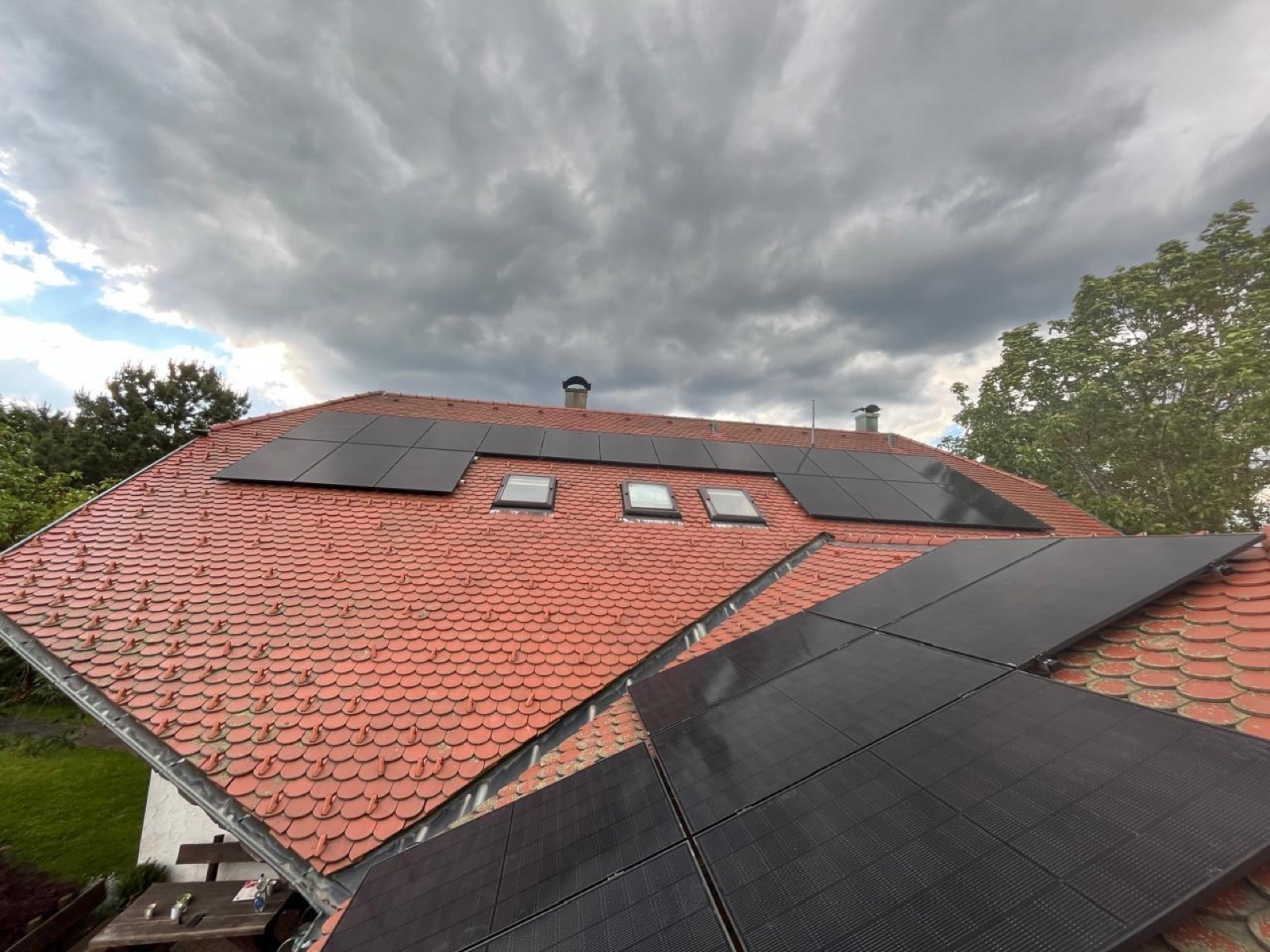 Aufdach-Photovoltaikanlage auf einem roten Tondach unter bewölktem Himmel